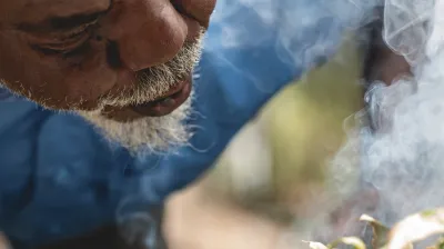 Ein älterer Mann mit grauem Bart führt eine traditionelle Rauchzeremonie durch