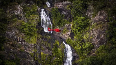 Roter Hubschrauber fliegt über einen Wasserfall im Regenwald