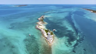 Tropische Insel mit weißem Sandstrand und Häusern im türkisfarbenen Meer.