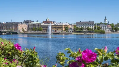 Häuser am See mit rosafarbenen Blumen im Vordergrund