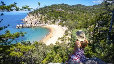 Frau betrachtet von einem Felsen aus eine wunderschöne Strandbucht.