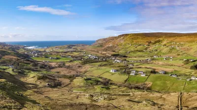 Grüne Hügellandschaft mit Häusern und Blick auf das Meer in Irland.