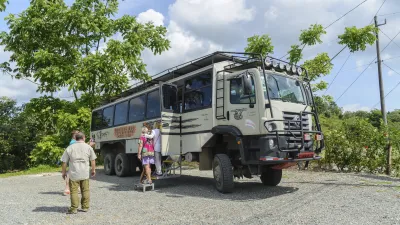 Geländegängiger Bus steht auf einem Kiesplatz mit Reisegruppe.