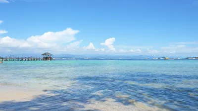Türkisblaues Meer mit einem Steg und Bergen im Hintergrund.