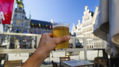 Ein Glas Bier wird vor dem Hintergrund historischer Gebäude gehalten.