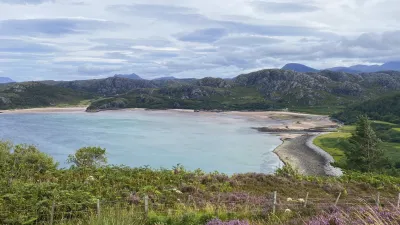 Gruinard Bay in Schottland zeigt einen Strand mit violetten Heideblumen.