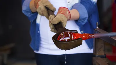 Ein Glasbläser formt flüssiges, rotes Glas mit Zangen.