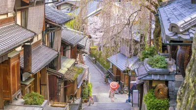 Historische Gassen in Kyoto mit traditionellen Holzhäusern und einer Frau mit rotem Sonnenschirm