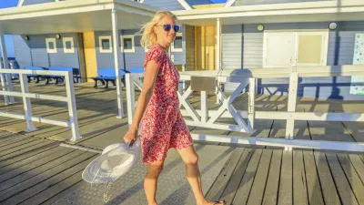 Eine Frau in rotem Kleid geht lächelnd auf dem Holzsteg.