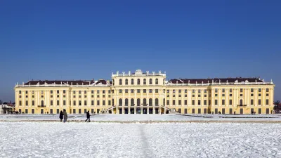 Schloss Schönbrunn im Winter mit verschneitem Vorplatz und blauem Himmel.